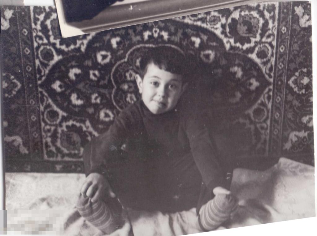 Маленький мальчик сидит на кровати на фоне ковра. Начало 1970-х гг.