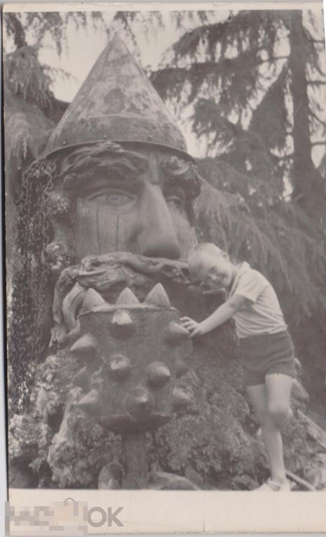Маленький мальчик в шортах у деревянной скульптуры богатыря. 1960-е гг.