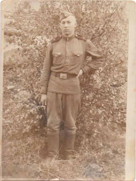 Солдат артиллерии Владимир стоит на фоне куста. 1954 г.