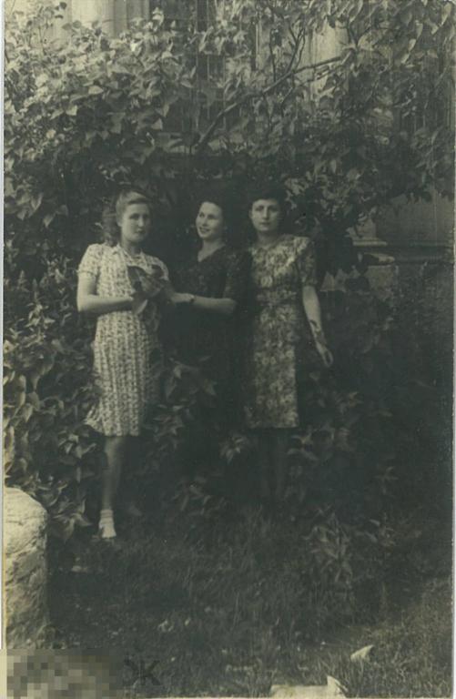 Три девушки в кустах на фоне стены дома. Днепропетровск, 1946 г.