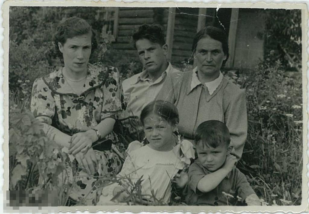 Семья сидит в траве на фоне деревянного дома. 1950-е гг.